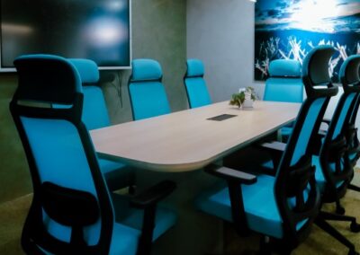 Modern meeting room with a table, office chairs, wall art, and a screen.