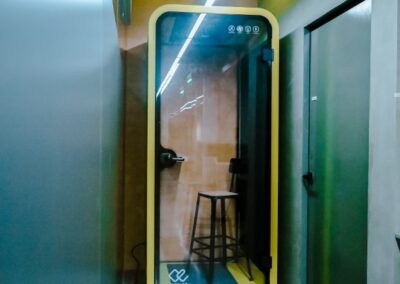 Soundproof phone booth with a stool in a modern office hallway.