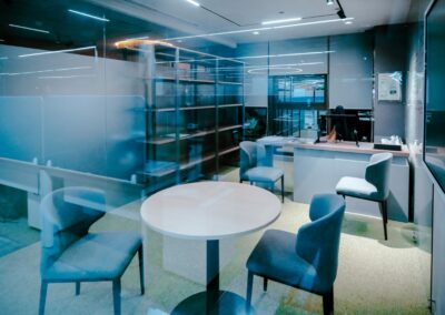 Small office meeting area with a round table, chairs, shelving, and a desk.