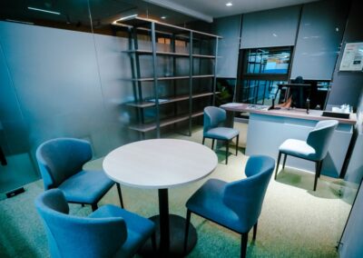 Small office meeting area with a round table, chairs, shelving, and a desk.