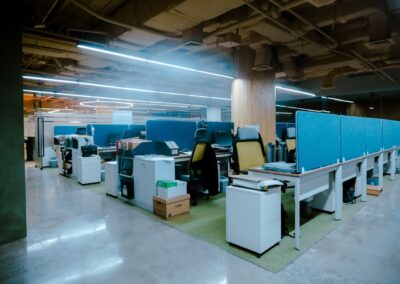 Open-plan office with desks, chairs, and overhead ductwork.