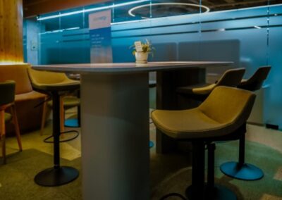 Modern office lounge with tables, chairs, and circular ceiling lighting.