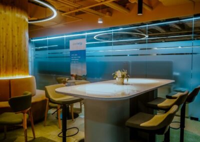 Modern office lounge with tables, chairs, and circular ceiling lighting.