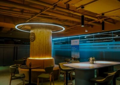 Modern office lounge with tables, chairs, and circular ceiling lighting.