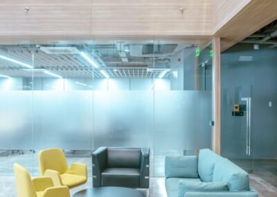 Office lounge with sofa, chairs, and a round table under a glass mezzanine.
