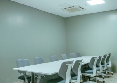 Small meeting room with a white table, rolling chairs, and ceiling-mounted projector.