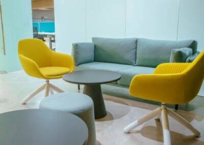 Lounge area with sofa, yellow chairs, and small tables.
