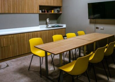 Office pantry with dining table, yellow chairs, and kitchenette.