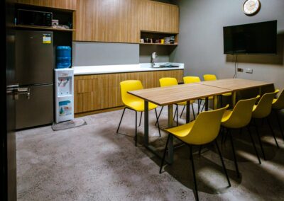 Office pantry with dining table, yellow chairs, and kitchenette.