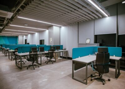 Open-plan office with rows of desks, blue dividers, and rolling chairs.