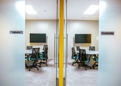 Glass meeting rooms with round tables and signs reading “Inclusive” and “Trustworthy”.