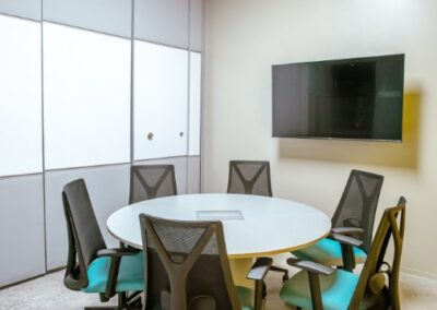 Small meeting room with round table, office chairs, and wall-mounted screen.