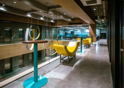 Open office walkway with yellow chairs and high tables.