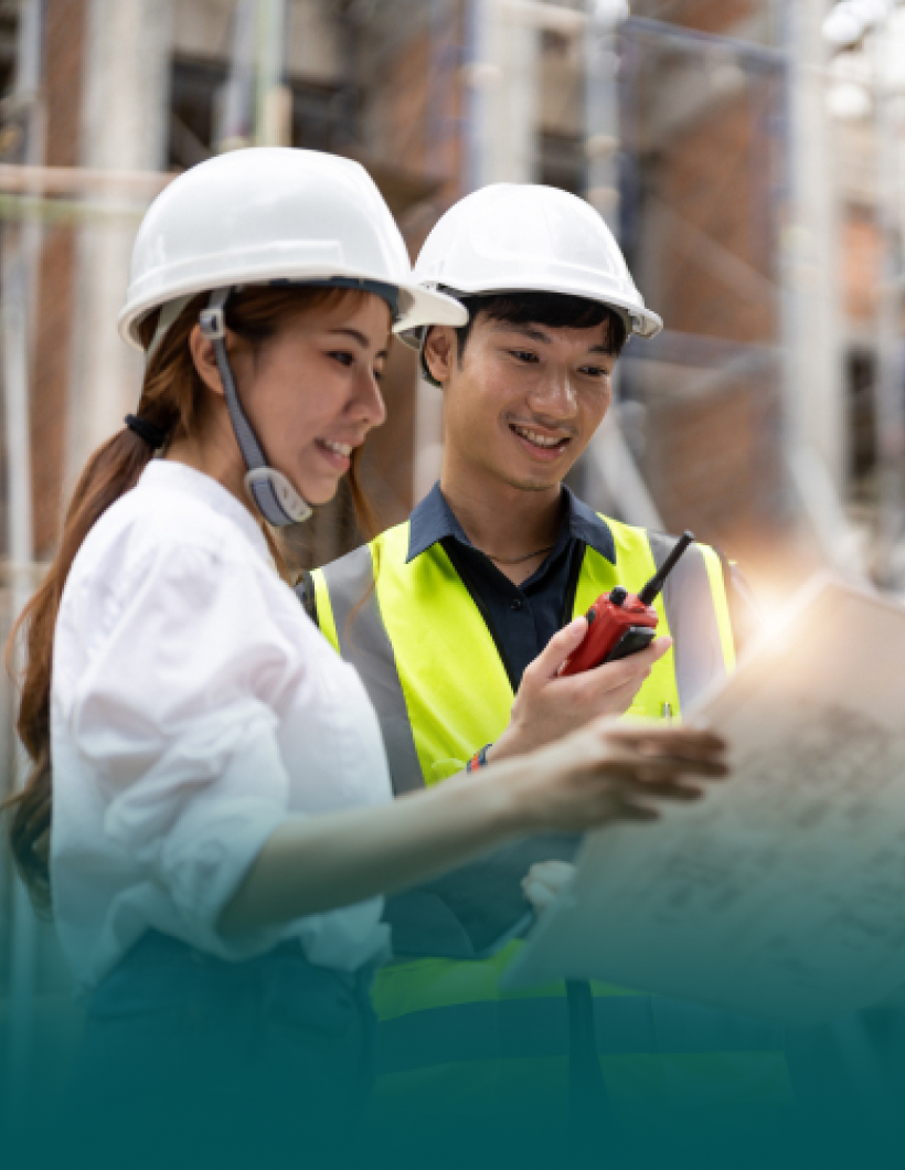 Construction workers reviewing plans and using a walkie-talkie on site.